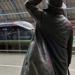 A Eurostar train in the station at St Pancras with a bronze statue of Sir John Betjeman, tipping his hat to the train, in the foreground.