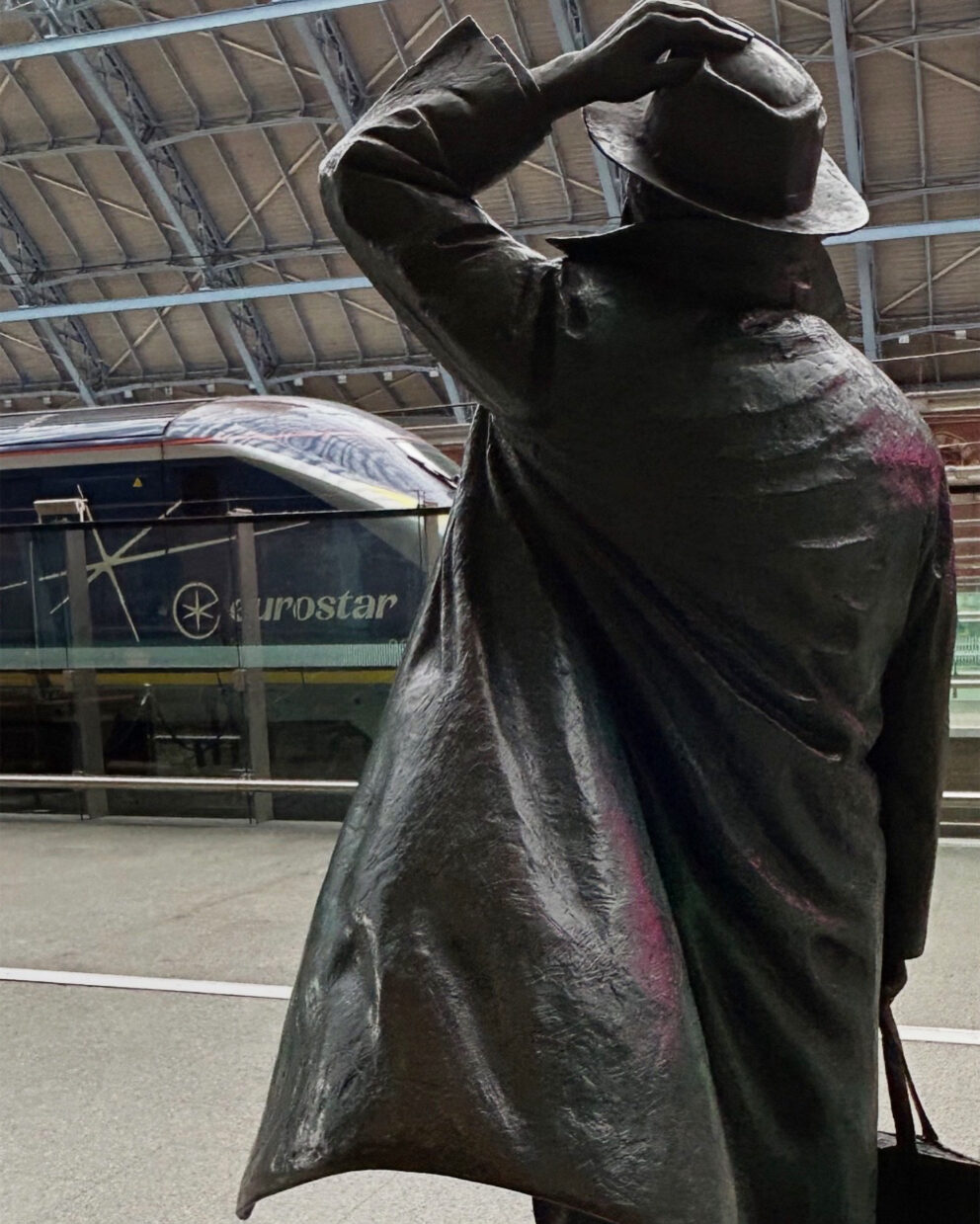 A Eurostar train in the station at St Pancras with a bronze statue of Sir John Betjeman, tipping his hat to the train, in the foreground.