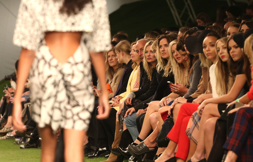 A model on the catwalk at London Fashion Week with front row spectators looking on.