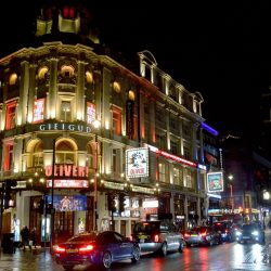 The exterior of the Gielgud Theatre in London at nighttime, with passing traffic.