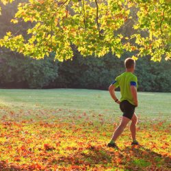 A man in shorts and tshirt, doing warm up exercises in a park on an autumnal day.